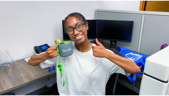 Nahli Smith, Felins Marketing Intern poses with a Felins branded mug and lanyard with a thumbs up and big smile