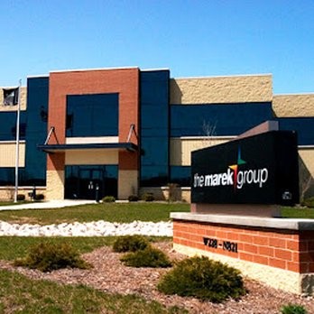 Exterior view of The Marek Group headquarters featuring a modern building with brick and glass facade, landscaped lawn, and prominent company signage at the front.