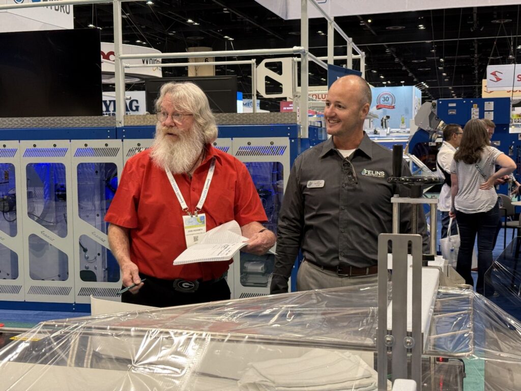 Felins Automation & Packaging expert, Joe McKillip (right), shows Felins laundry automation systems to a booth visitor (left) at the CLEAN show 